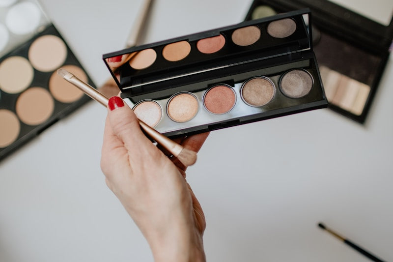 Main tenant un pinceau devant une palette de fards